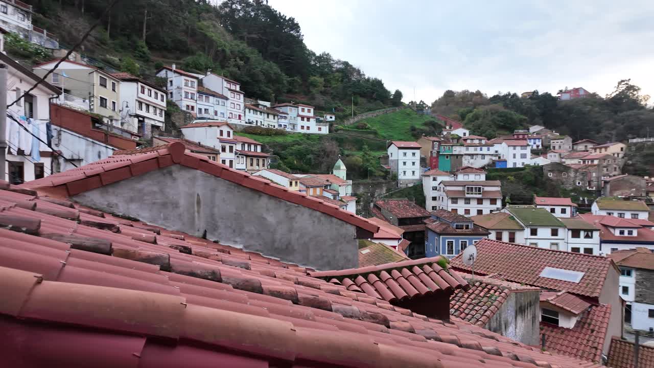 Panorama elevado em câmera lenta de Cudillero, mostrando casas na encosta e litoral sob luz do dia nublada