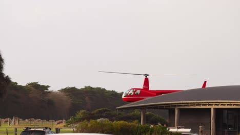 red helicopter taking off near a building