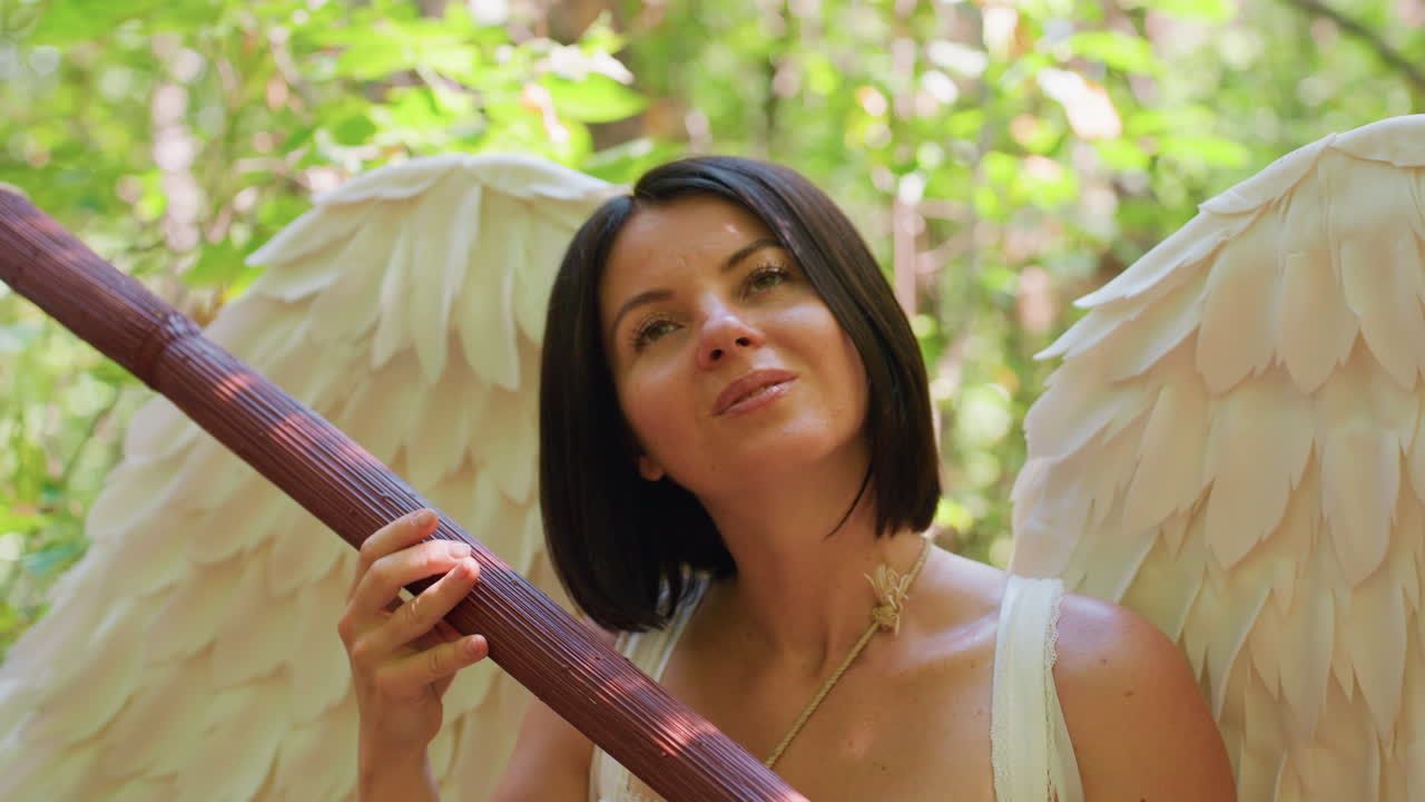 Serene lady in angel costume with white wings holding wooden staff like harp, eyes closed in peaceful meditation amid glowing forest light, expressing divine calm, purity, and spiritual harmony