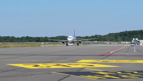 avión estacionado en la plataforma del aeropuerto con vagón de equipajes y cargador de cinta de equipaje del aeropuerto conduciendo al costado del aeropuerto de eindhoven en los países bajos