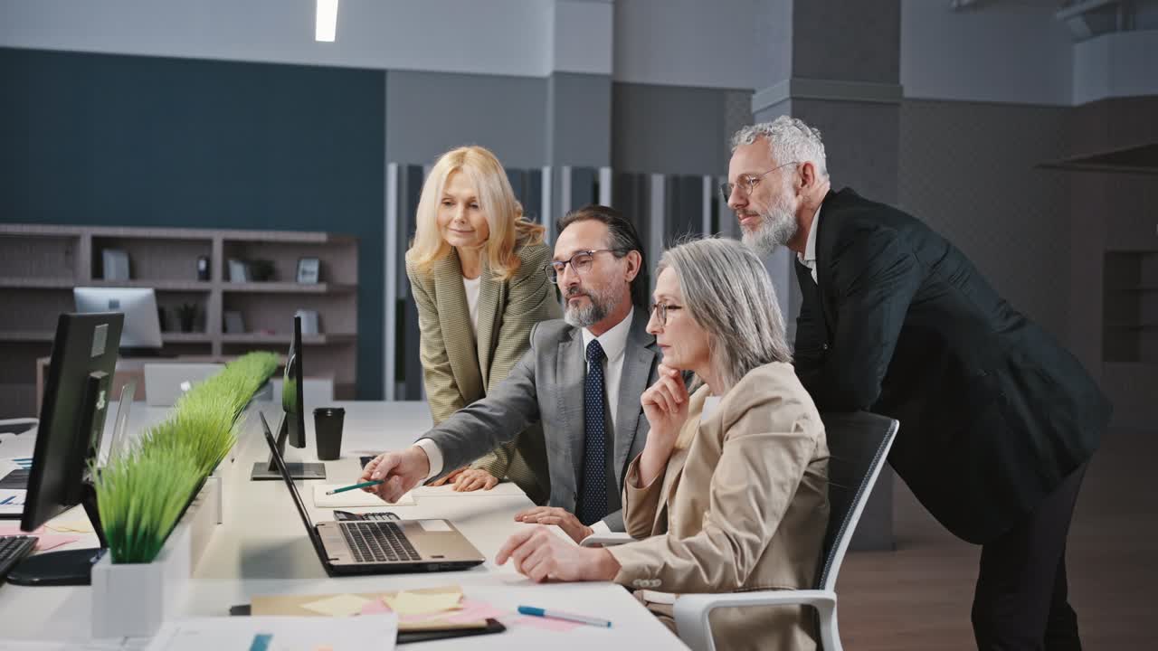 профессиональный зрелый мужчина сотрудник показывает план на ноутбуке коллегам, обсуждает проект в офисе, отслеживает выстрел