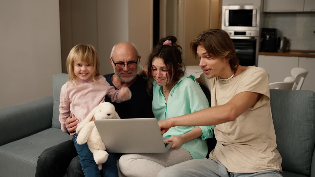 los niños y el abuelo están riendo juntos mientras usan una computadora portátil, viendo video