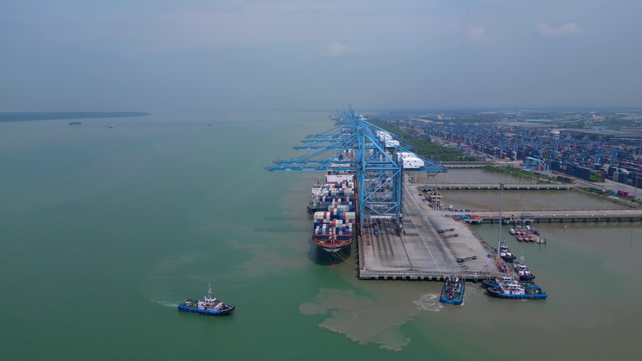 large container ship docked at Northport terminal with gantry cranes, illustrating global logistics and maritime trade. Beautiful aerial view dolly left drone