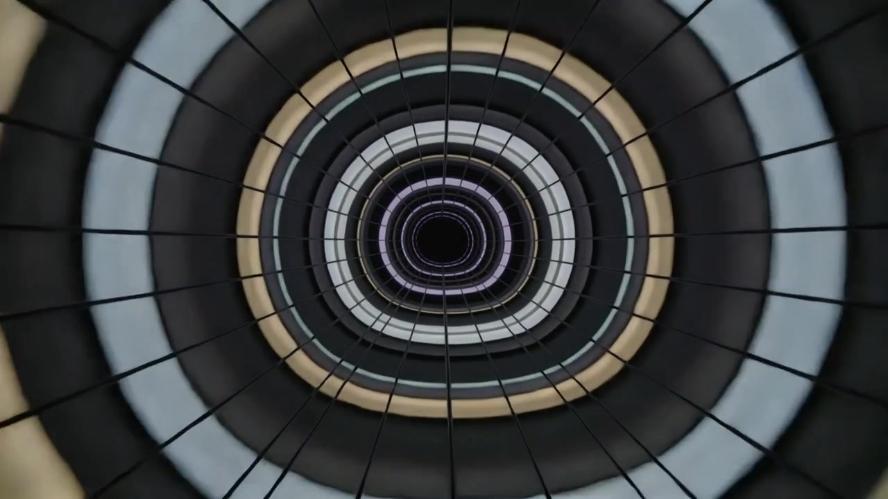 Telecamera che zooma e sale in un atrio, con cambiamenti di colore che iniziano lo zoom verso anelli concentrici e un vuoto oscuro.