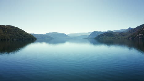 low forward aerial over still water by forested hills in argentina