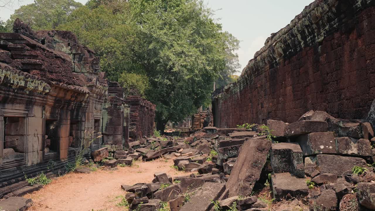 Vista del corridoio di un antico tempio con pietre cadute, mura in rovina e alberi ad Angkor Wat in Cambogia, che mostra l'architettura storica, il degrado e il patrimonio culturale
