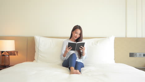 Una-Mujer-Joven-Y-Atractiva-Disfruta-De-Un-Momento-De-Tranquilidad-Mientras-Se-Sienta-En-La-Cama-De-Su-Suite-De-Hotel-Leyendo-Un-Libro