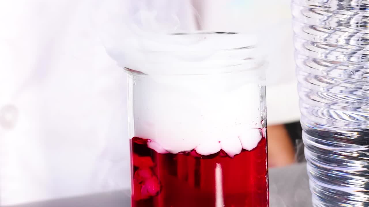 A jar with red liquid produces white smoke, captured in a bright setting.