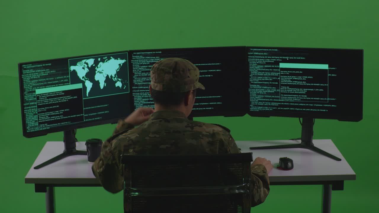 지루한 아시아인 병사의 뒷모습 개발자는 그린 스크린 스튜디오에서 여러 컴퓨터 화면으로 코드를 작성합니다.