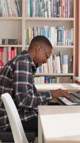 happy man plays synthesizer at home. smiling black musician rehearses melody on electrical instrument by bookcase. african american guy performs music