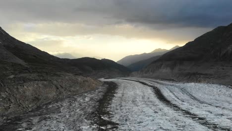 Aerial-flyover-over-the-longest-glacier-in-the-Alps---the-Aletsch-glacier-in-Valais,-Switzerland---with-view-of-the-sunset-at-the-end-of-the-glacier