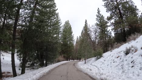 Driving-to-a-winter-wonderland-in-the-Tehachapi,-California-mountains-along-a-remote-road-with-snow-on-the-ground---rear-view