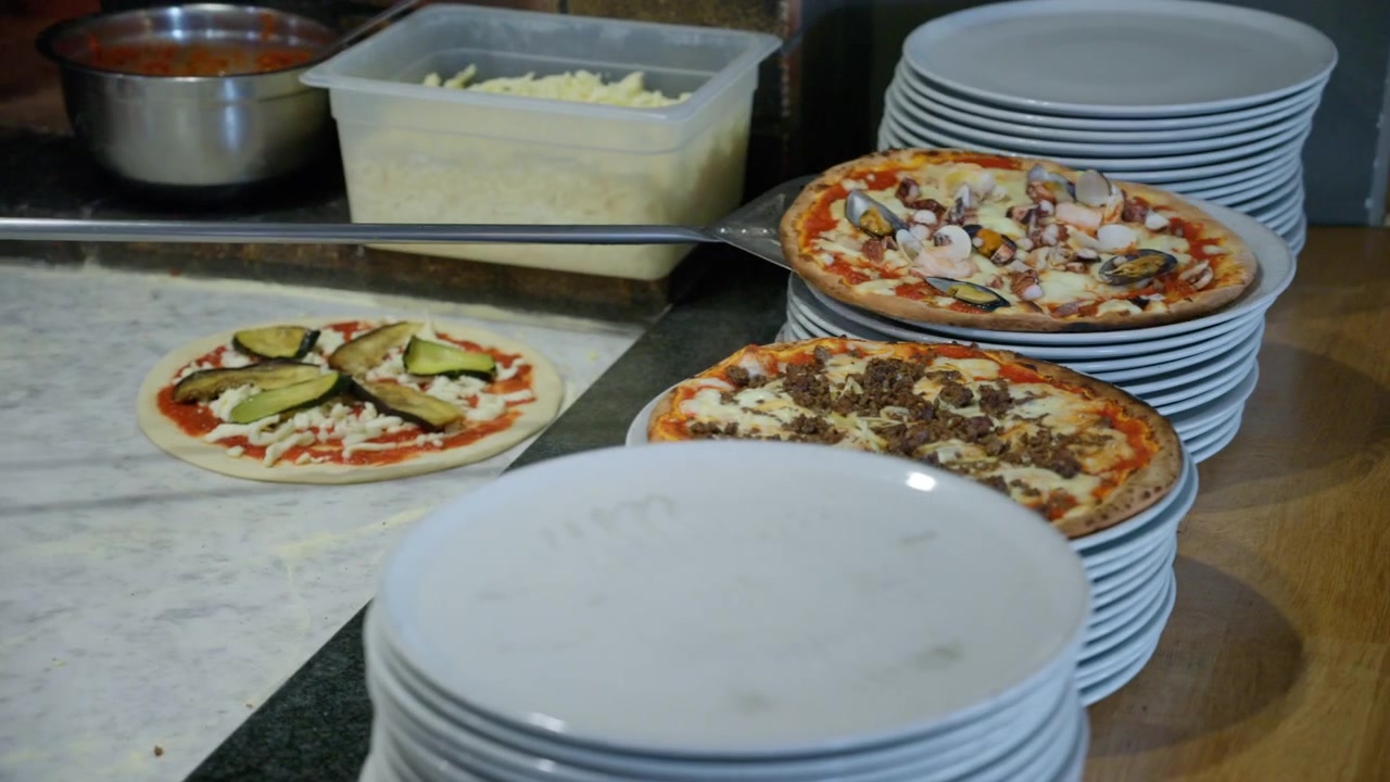 Pizza che cuoce all'interno di un forno a legna in mattoni caldo, mostrando il processo di cottura tradizionale del cibo italiano. Ingredienti nelle vicinanze