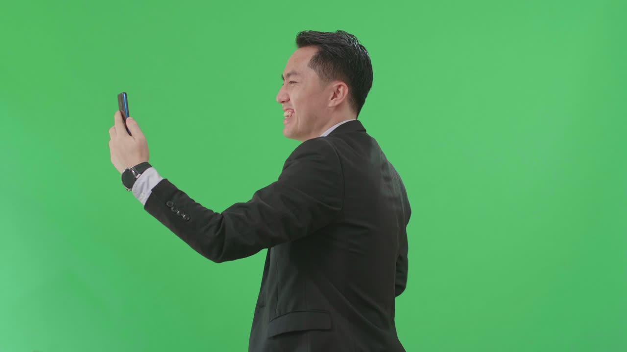 Side View Of Asian Business Man Having Video Call On Mobile Phone While Walking On Green Screen Chroma Key