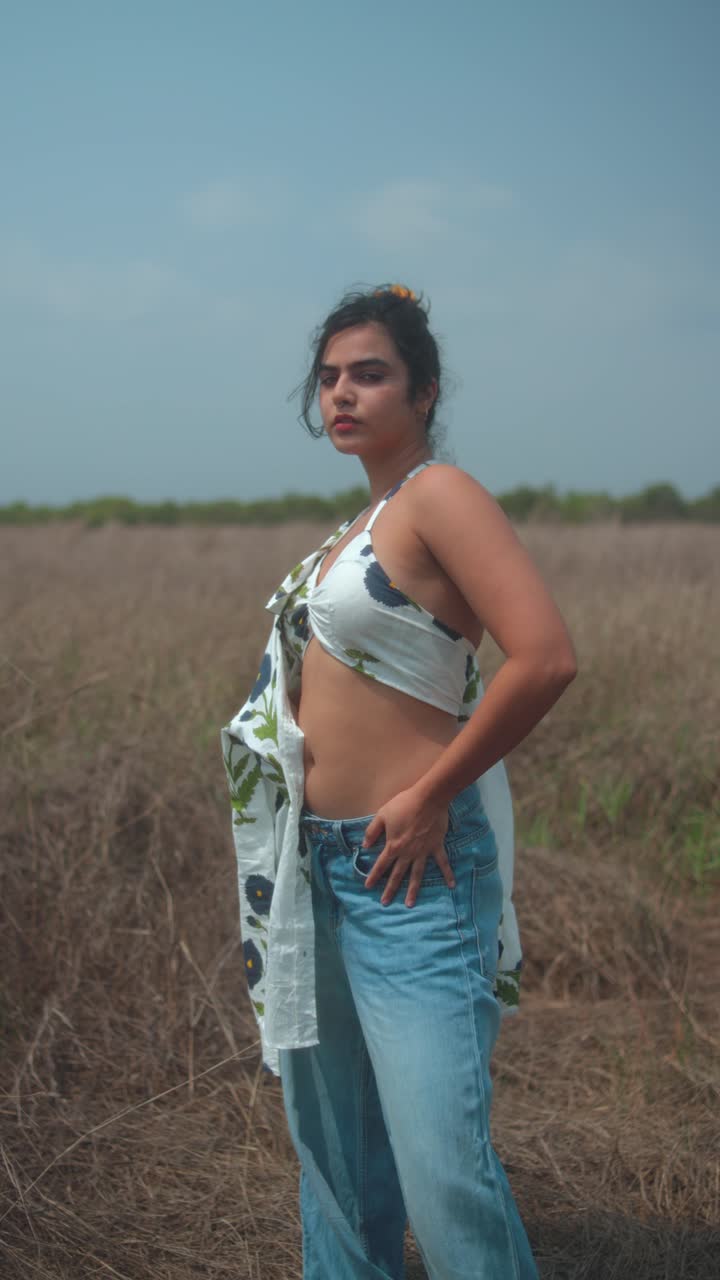 Young woman posing in a field wearing a floral top and jeans with confidence