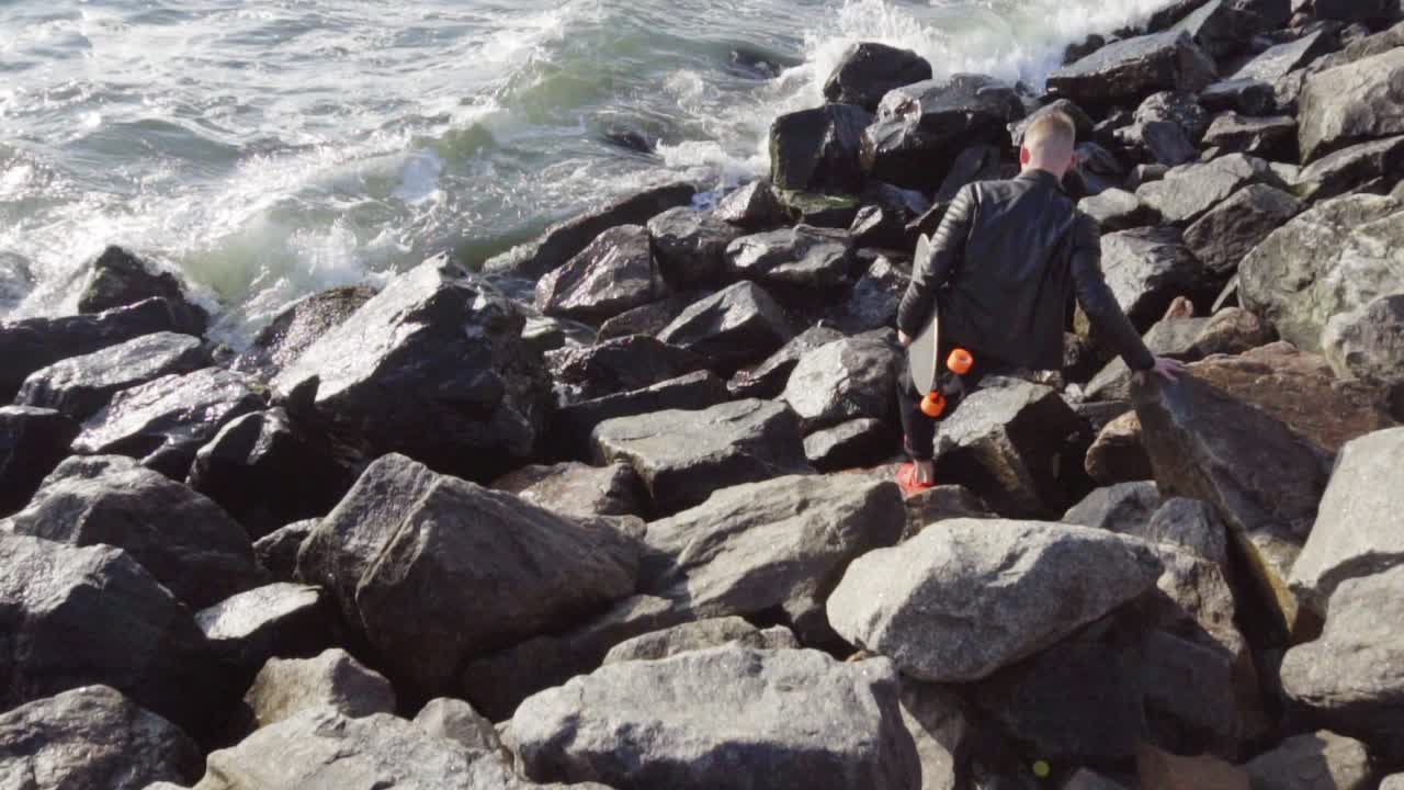 젊은 남자가 그의 롱보드를 들고 바다로 내려갑니다.