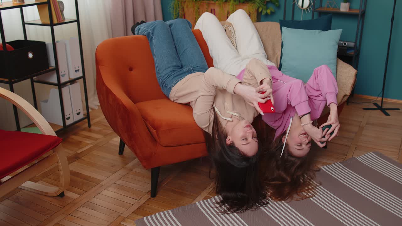 두 명의 재미있는 소녀 친구 형제 자매가 스마트폰에서 열정적으로 경주 비디오 게임을 하고 있습니다.