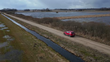 Red-SUV-driving-over-a-sandy-road-on-a-cloudy-day-in-Poland