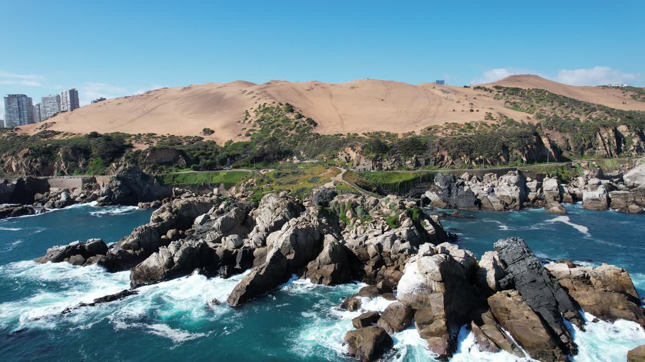 Traveling Shot from Breaking Waves on the Rocks of the Coast with Dunes in the Background and some buildings, Vi&ntilde;a del Mar, Chile