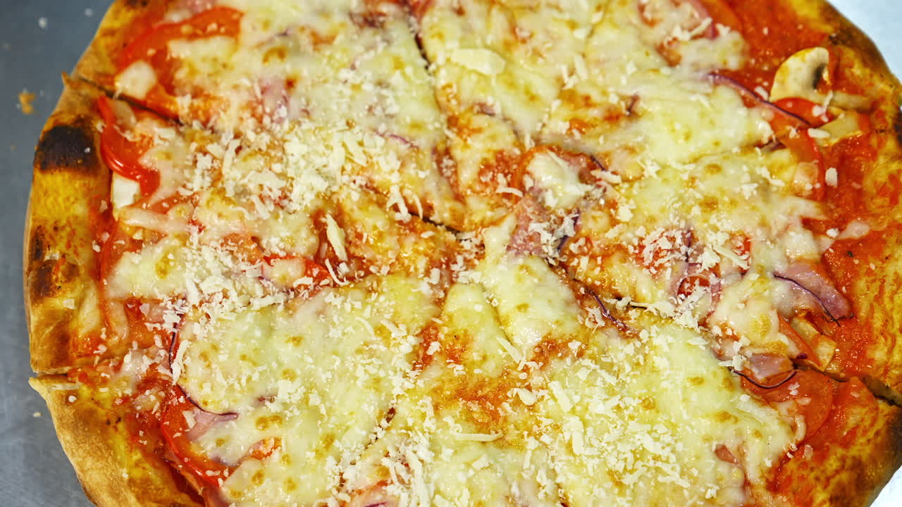 Ready pizza is sprinkling with cheese. Well baked pizza with melted cheese and other ingredients. Tasty snack. Close-up. Top view.
