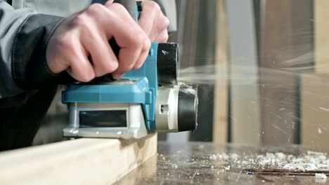 close-up of a carpenter's hand working with an electric plane in a home workshop