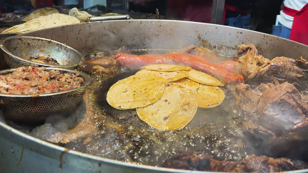 Carni tradizionali messicane di suadero e longaniza che sfrigolano su una piastra professionale da street food a Città del Messico.