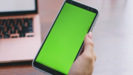 una mujer irreconocible usando un teléfono inteligente con pantalla verde en el lugar de trabajo de cerca.