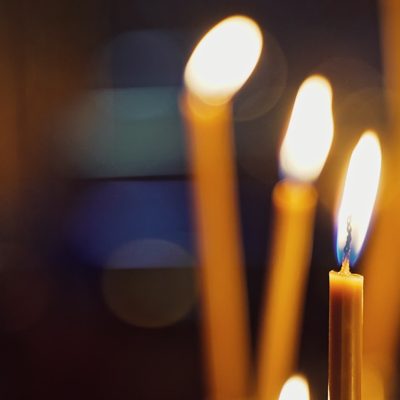Bright candles are glowing on the blurred background. Church candles burning in the night temple. Candles flame.
