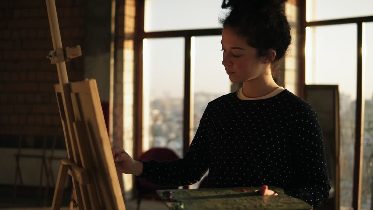 Fully concentrated sophisticated female artist in her 20's is drawing picture on easel. Slow motion rotating fotage.