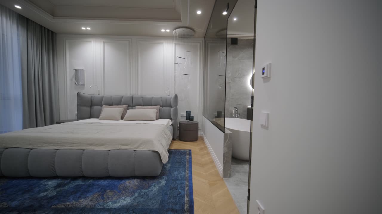 Luxurious bedroom with a tufted headboard and integrated bathroom featuring a freestanding bathtub and illuminated mirror