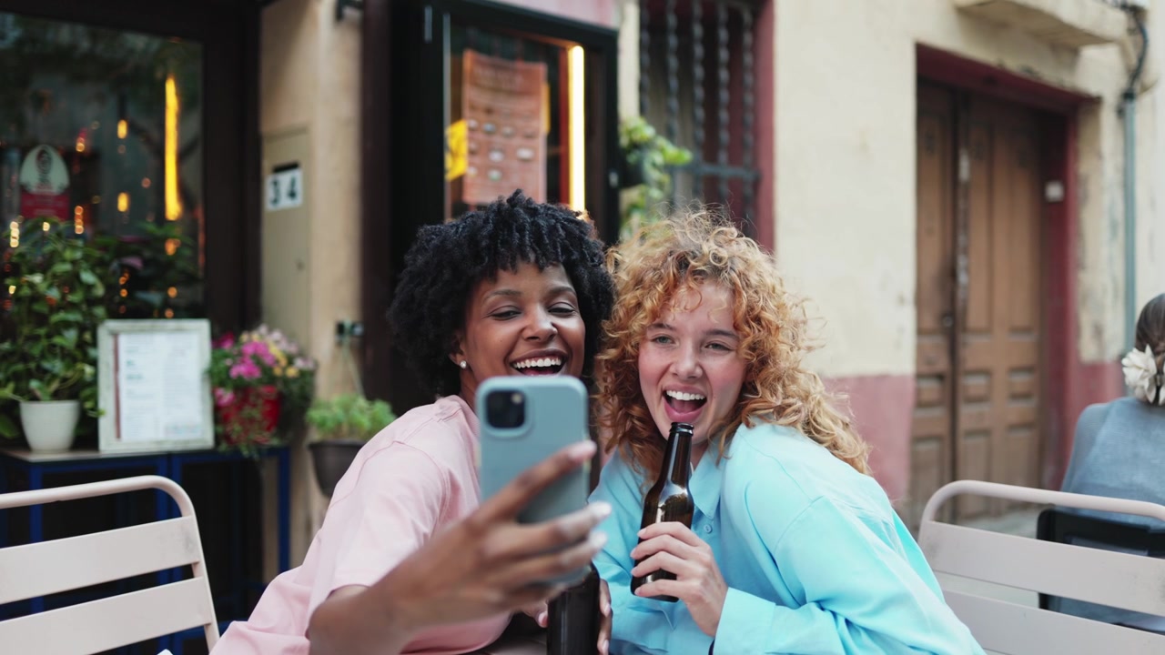 Due donne felici di diverse etnie che si scattano un selfie in un caffè all'aperto