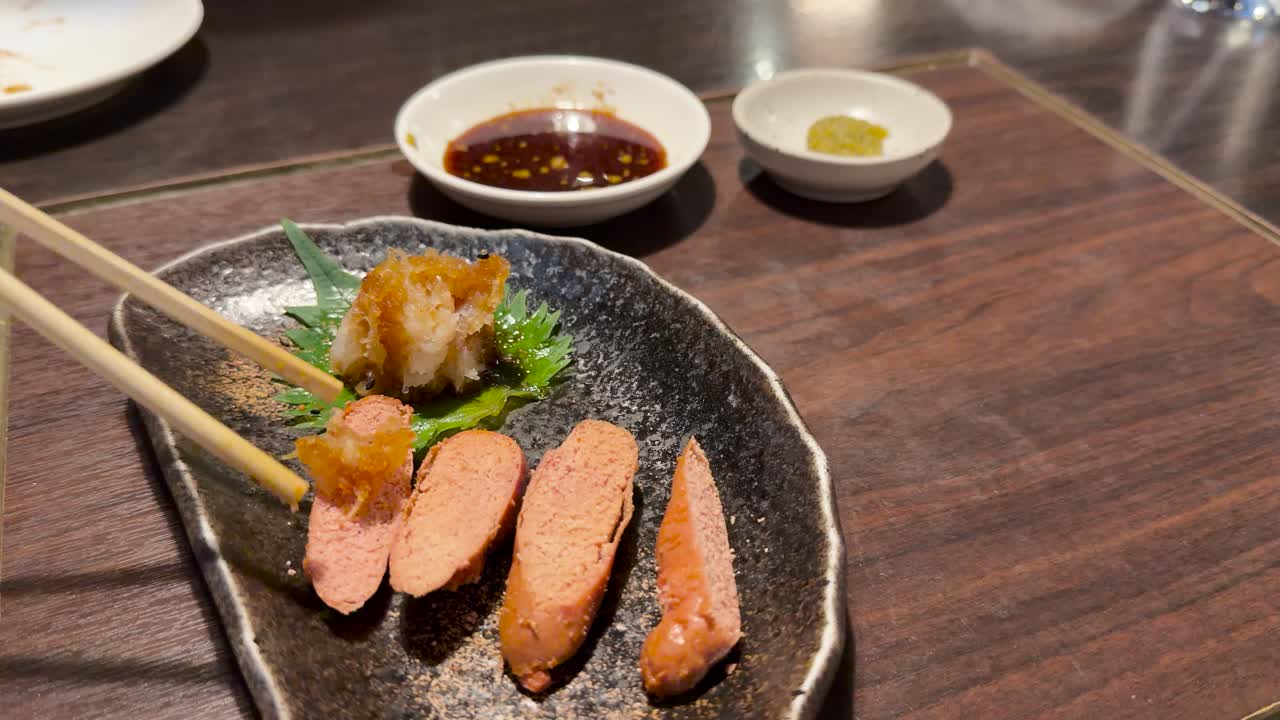 Chopsticks lift seafood from ceramic plate, warm indoor lighting, wooden table, shallow depth of field