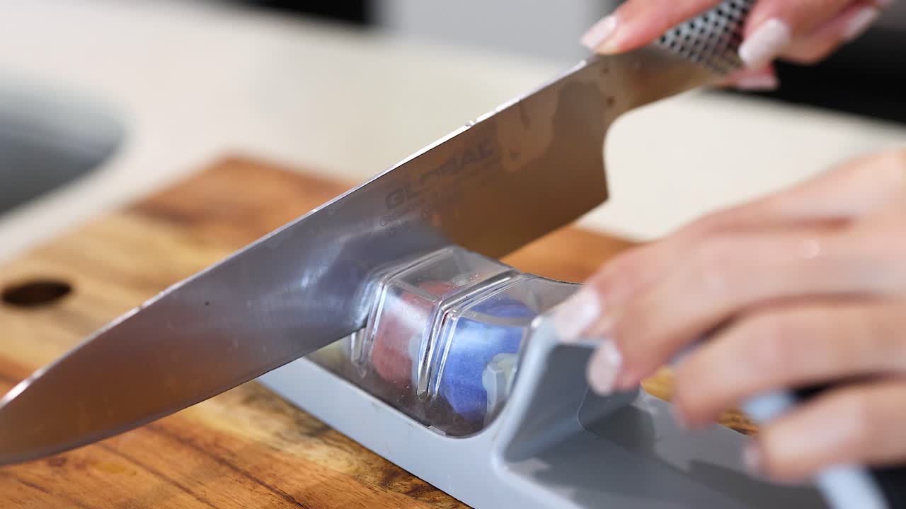 Hands sharpening a knife on a stone in a well-lit kitchen environment, focusing on precision and technique