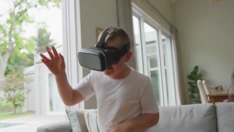 smiling caucasian boy standing in living room and using vr headset at home