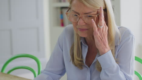 Reife-Frau-In-Den-Wechseljahren-Mit-Brille,-Die-Zu-Hause-Am-Laptop-Arbeitet-Und-Unter-Kopfschmerzen-Leidet