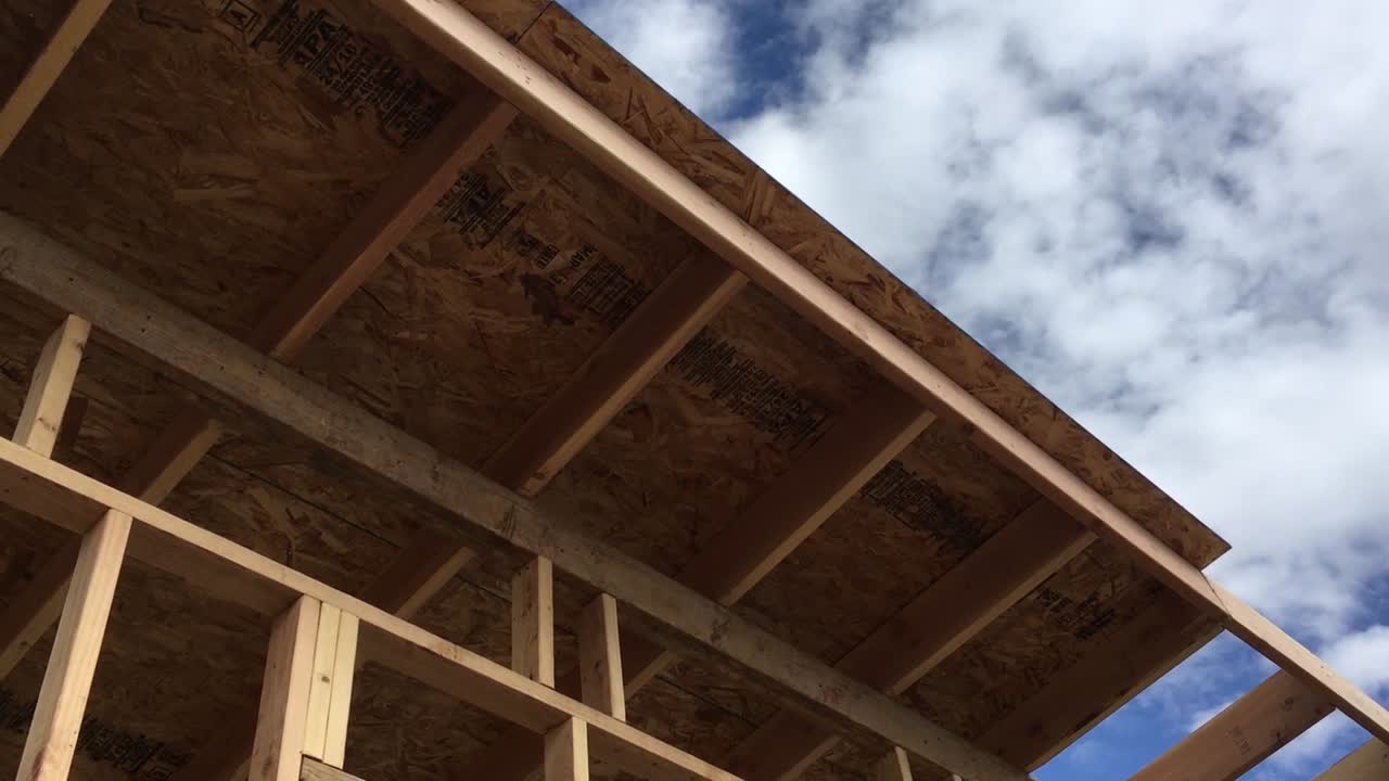 Construction worker sliding a piece of plywood into place on roof against blue sky on sunny day