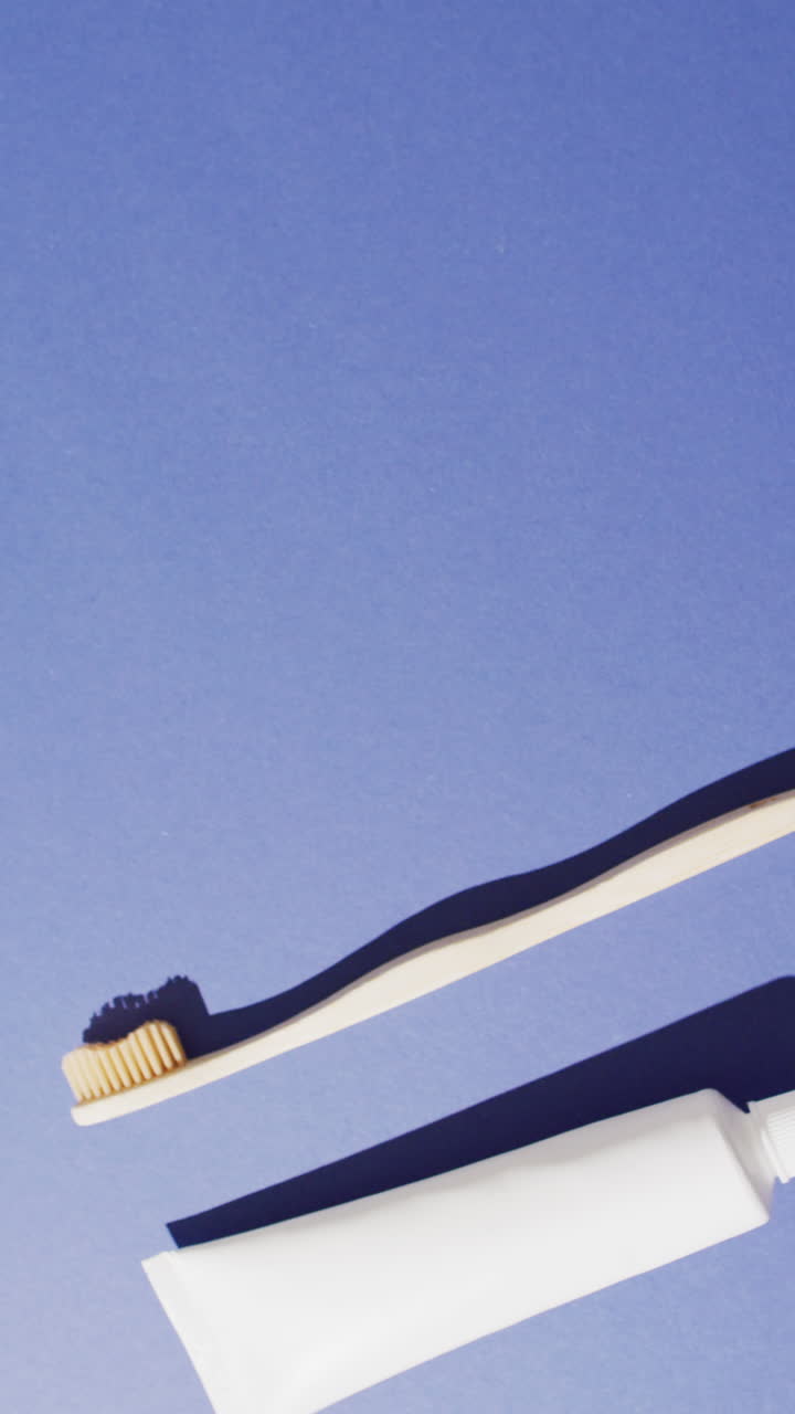 Vertical video of toothpaste and toothbrush on blue background with copy space