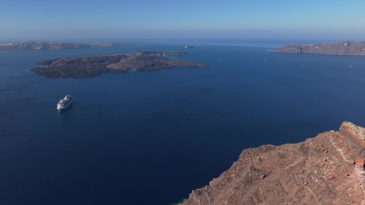 Vista panorámica de la caldera de Santorini y el mar Egeo de un azul profundo mientras el dron realiza una suave guiñada, revelando los dramáticos acantilados volcánicos y el icónico paisaje isleño