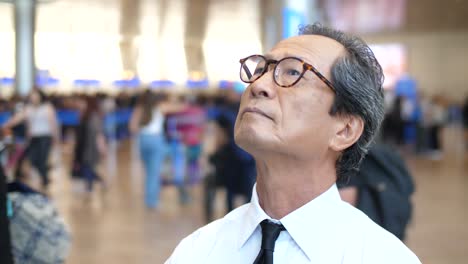 일본인 사업가 가 이스라엘 의 벤 구리온 공항 에 서서 도착 및 출발 보드 를 보고 있다. 그 는 안경 에 반사 되어 앞 에서 사진 을 찍고 있다.