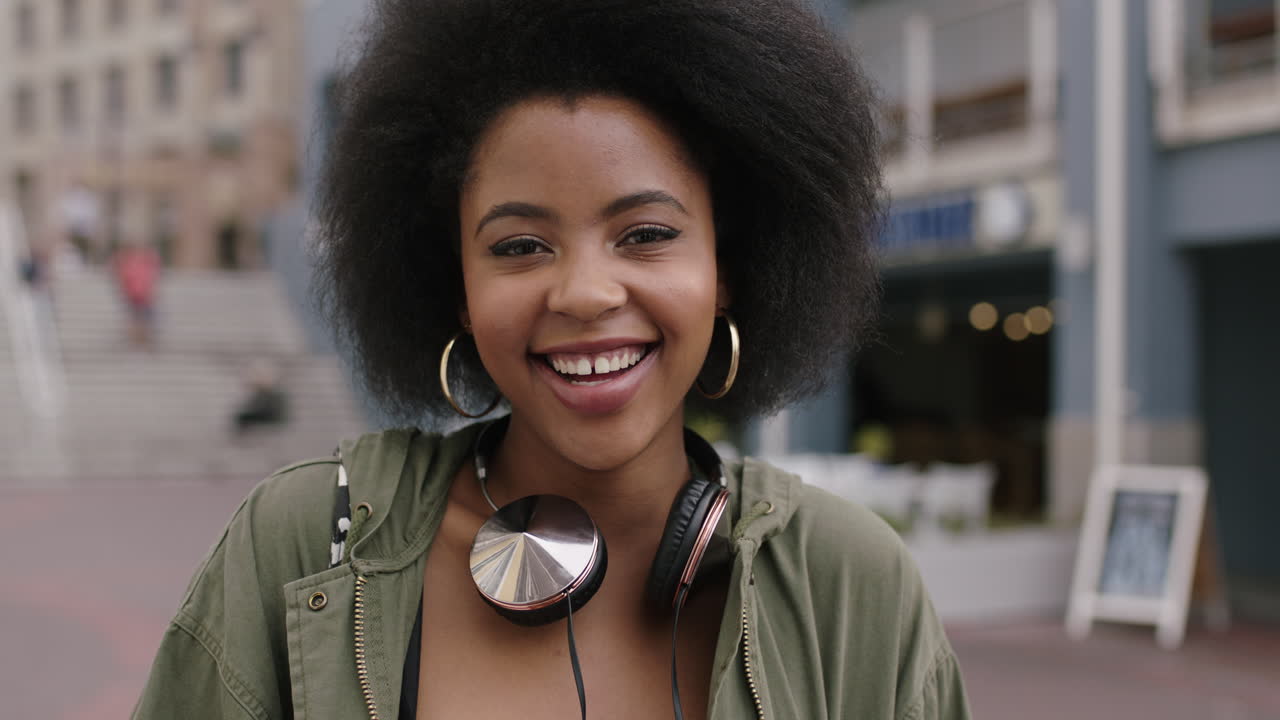 retrato en cámara lenta de una joven mujer afroamericana de moda con cabello afro rizado sonriendo feliz al aire libre urbano