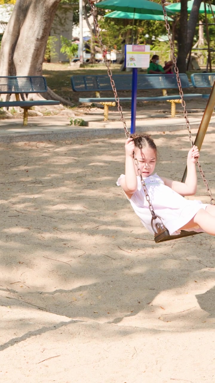 Una giovane ragazza asiatica dondola felicemente su un parco giochi a Lumpini Park, Bangkok, Thailandia