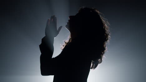 silhouette woman praying in darkness. believer girl whispering prayer indoors.