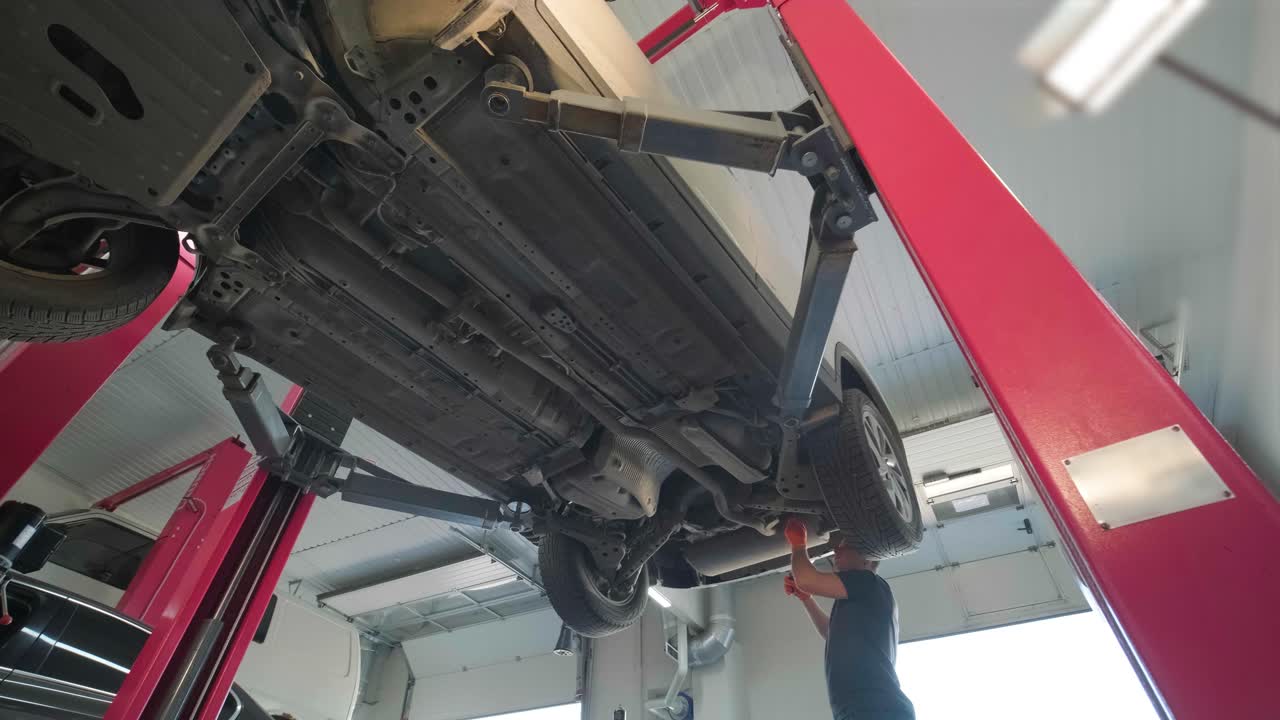 joven mecánico profesional que trabaja bajo el coche moderno levantado en el servicio de reparación de automóviles. servicio de automóviles, mantenimiento de reparación.