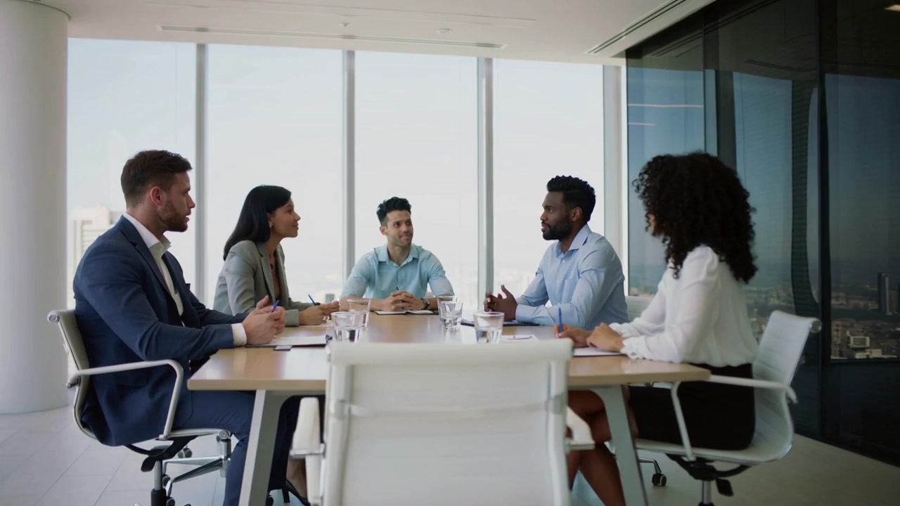 Palestrante em traje de negócios iniciando reunião, conduzindo a conversa e gesticulando no escritório, com a equipe usando cadernos.