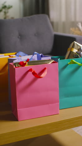 Vertikales-Video-Eines-Mannes,-Der-In-Geschenkpapier-Verpackte-Geschenke-In-Bunten-Tüten-Mit-Etikett-Auf-Einem-Tisch-Im-Wohnzimmer-Zu-Hause-Aufhebt