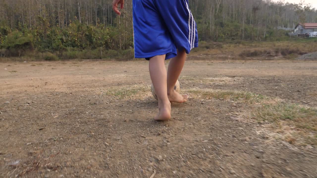 Boy playing soccer barefoot in a rural field