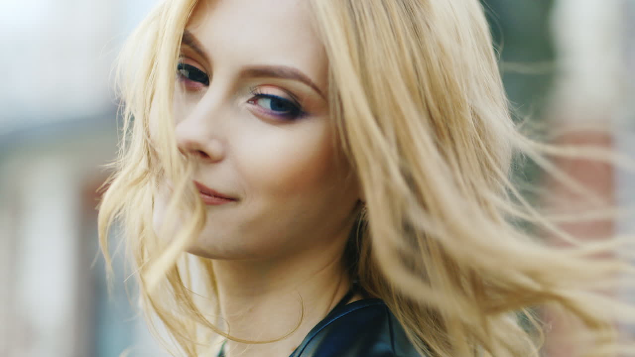 молодая женщина улыбается в камеру, флиртуя, ветер развевает ее волосы