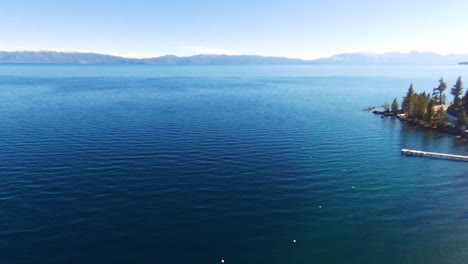 Toma-Panorámica-Aérea-Del-Lago-Tahoe-Junto-Con-árboles-Verdes-Y-Nieve-En-Un-Día-Soleado