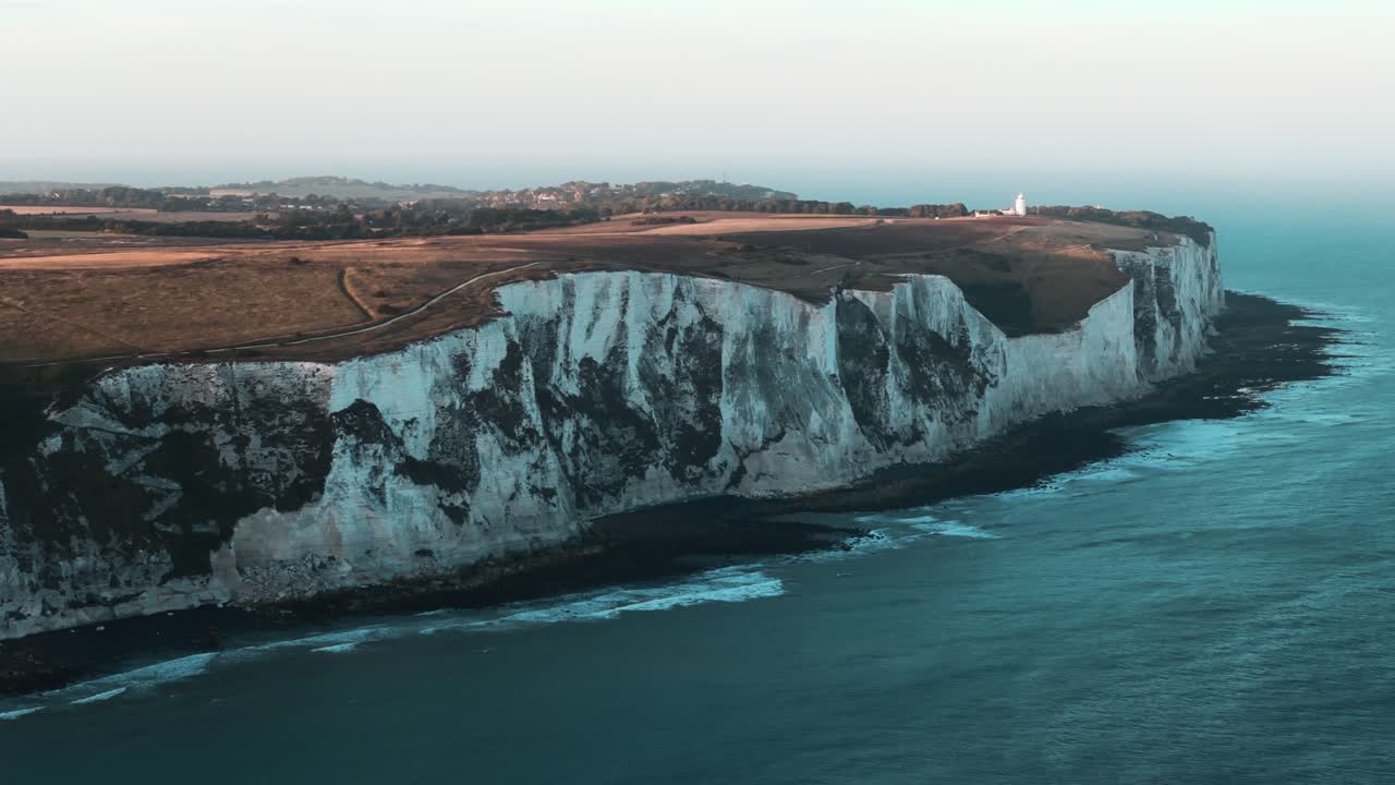 Rightward drone circle reveals full edge of Cliffs of Dover over turquoise water, establishing aerial backdrop overview