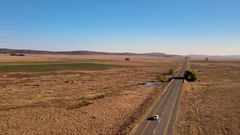 Remote-countryside-on-an-open-road-with-a-lonely-car,-farm-lands,-and-clear-skies---South-Africa